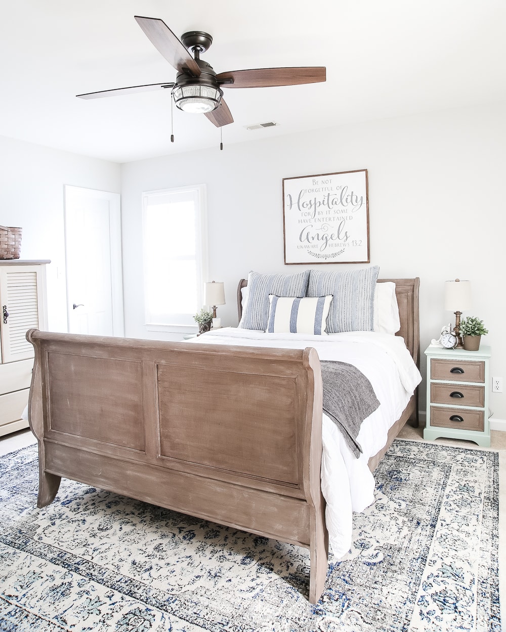 Wooden sleigh bed with white sheets and wooden ceiling fan.