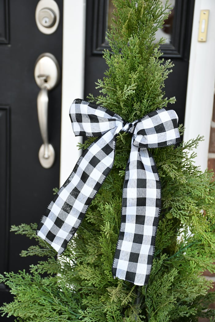 Large tree planters with a checkered bow tied around it by the front door.