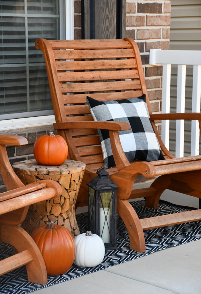 Wooden chairs, black and white pillows, white and orange pumpkins and a black and white rug on front porch.