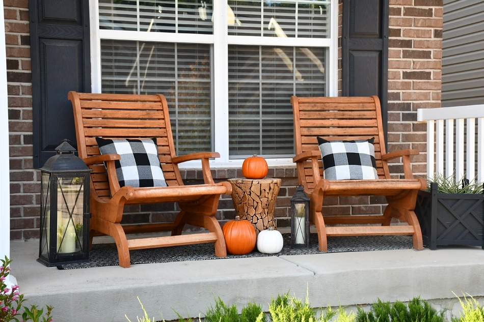 Two wooden chairs on the fall front porch with black and white checkered pillows on them.