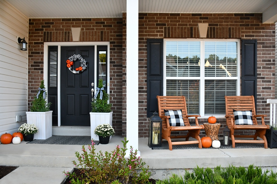 Front porch with black door and two chairs decorated for fall.