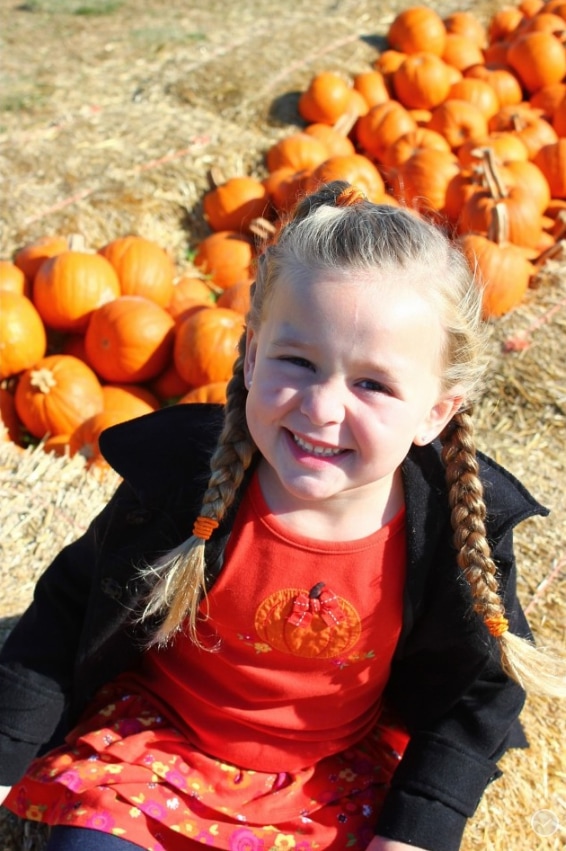 Girl with braids sitting by a row of pumpkins.