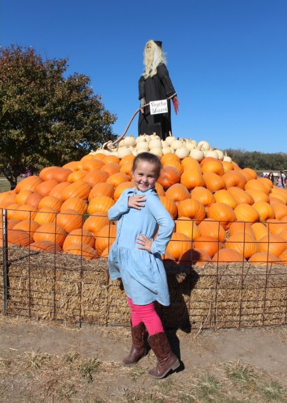 Girl in jean dress in front of pumpkin display.