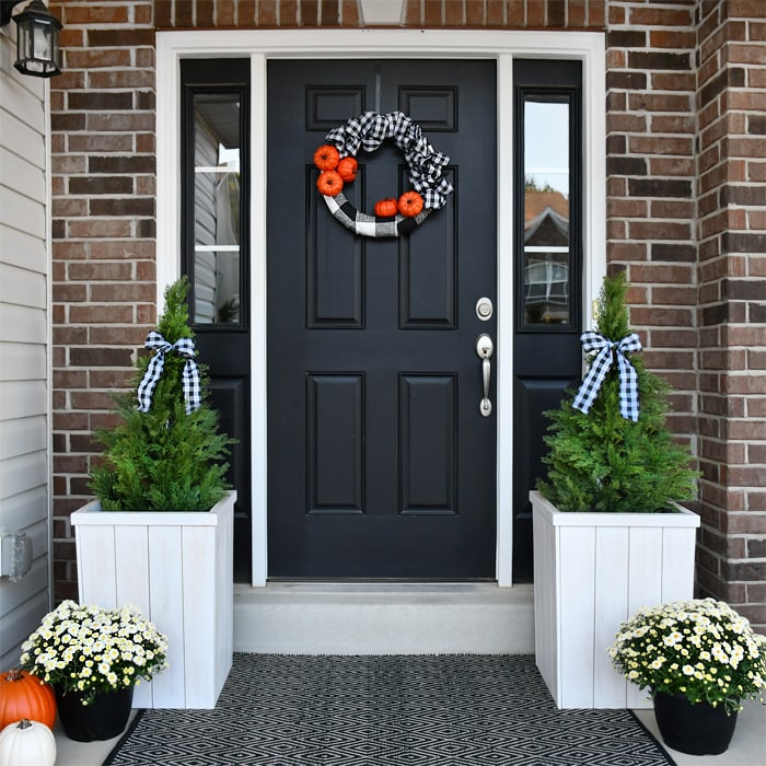 Black front door with a pumpkin and checkered wreath on it.