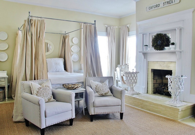 A 4 poster bed with fireplace and 2 armchairs in master bedroom.