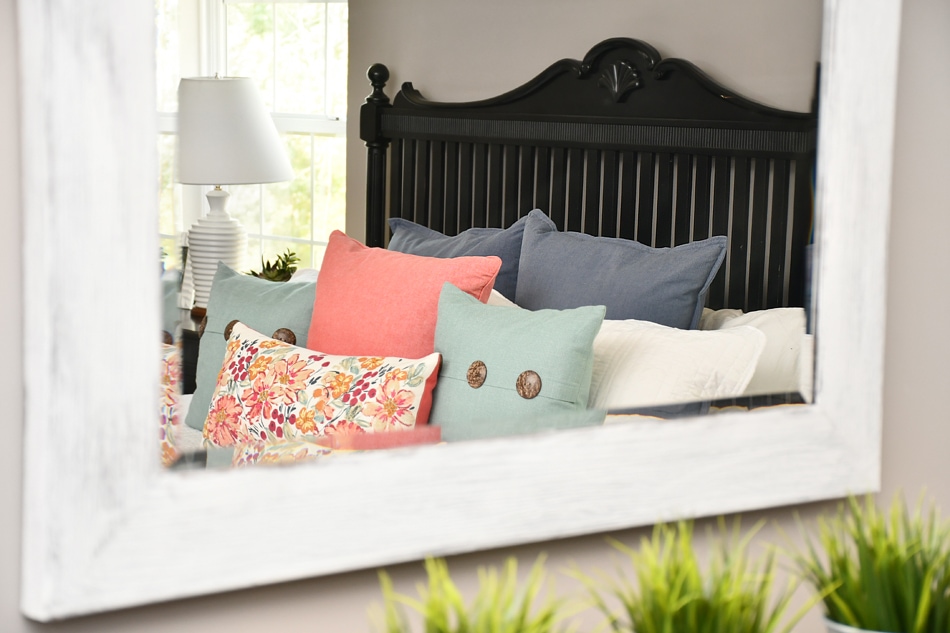 Black bed frame and pink, blue and peach pillows on bed in master bedroom.