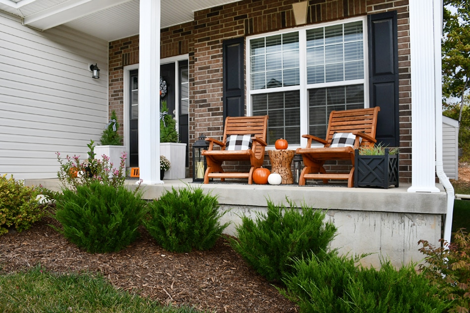 Front porch of house with chairs and pillows on chairs and pumpkins.