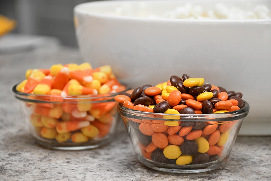 Reeces pieces and candy corn in clear bowls on counter.