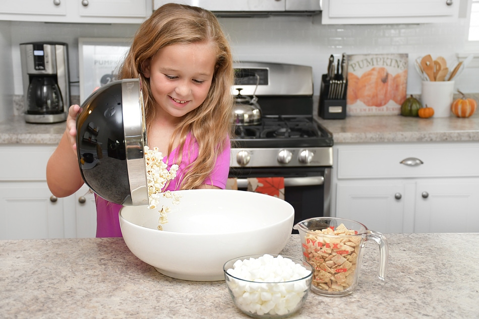 Little girl putting popcorn into a bowl.