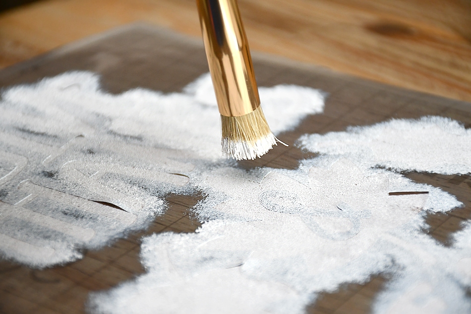 Stenciling the white paint with a brush on the cutting board.