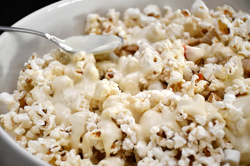 Using a spoon to pour melted white chocolate over the popcorn.