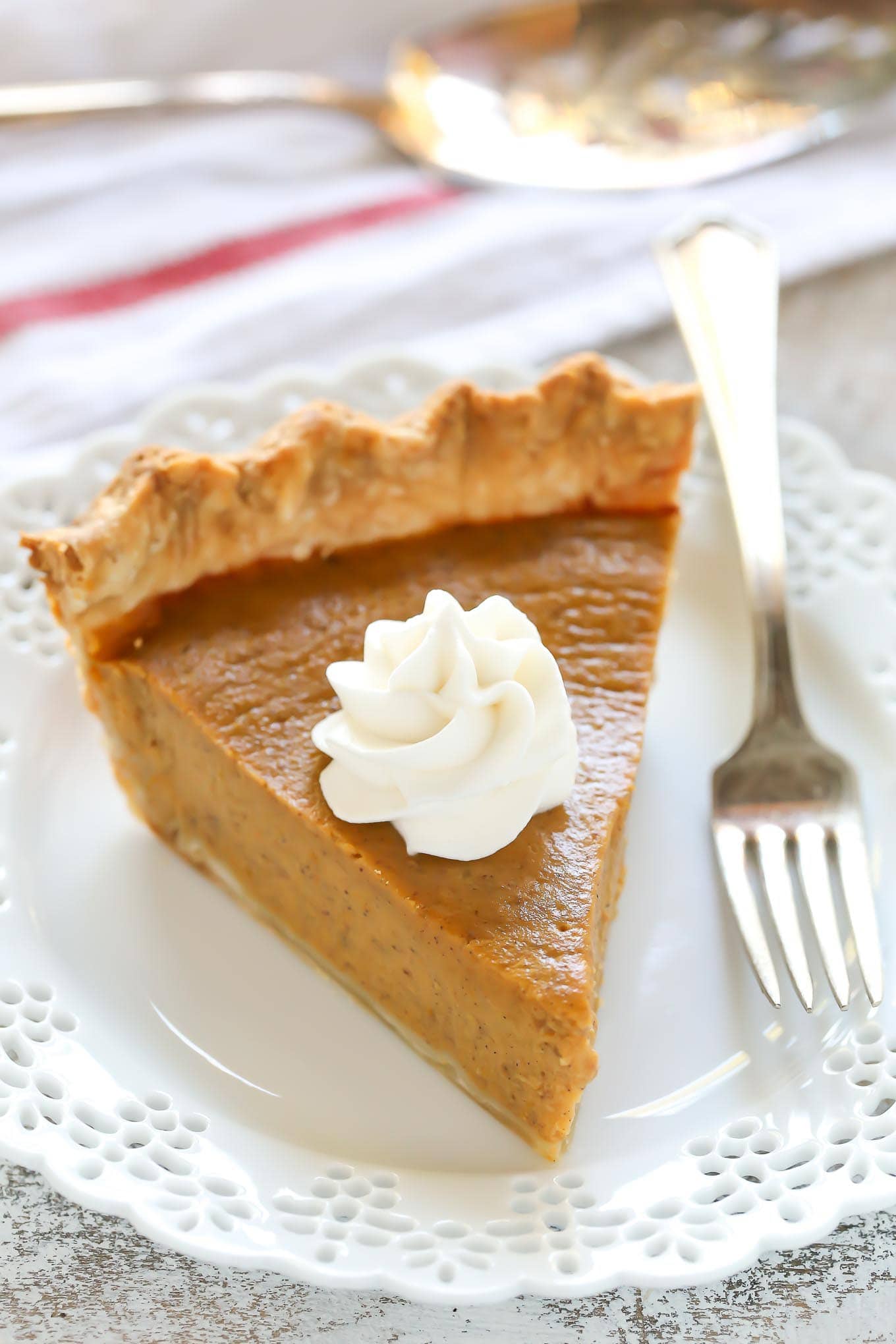 Pumpkin pie on a white plate, a dollop of whip cream on top and a fork beside it.