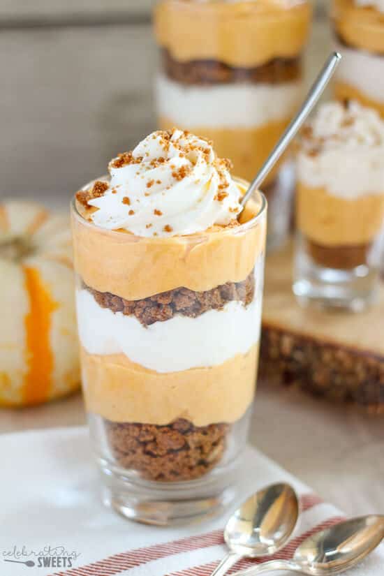 A glass cup with layers of crunchy bits, cream and pumpkin cream and a spoon in the glass.
