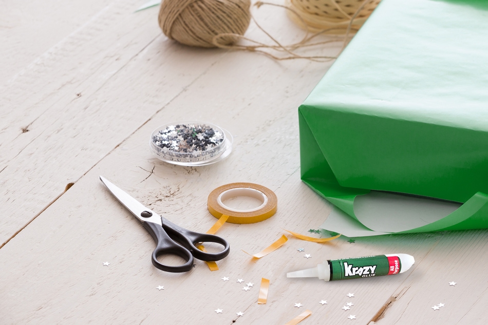 Scissors, twine, a half wrapped present, tape and Krazy Glue beside them.