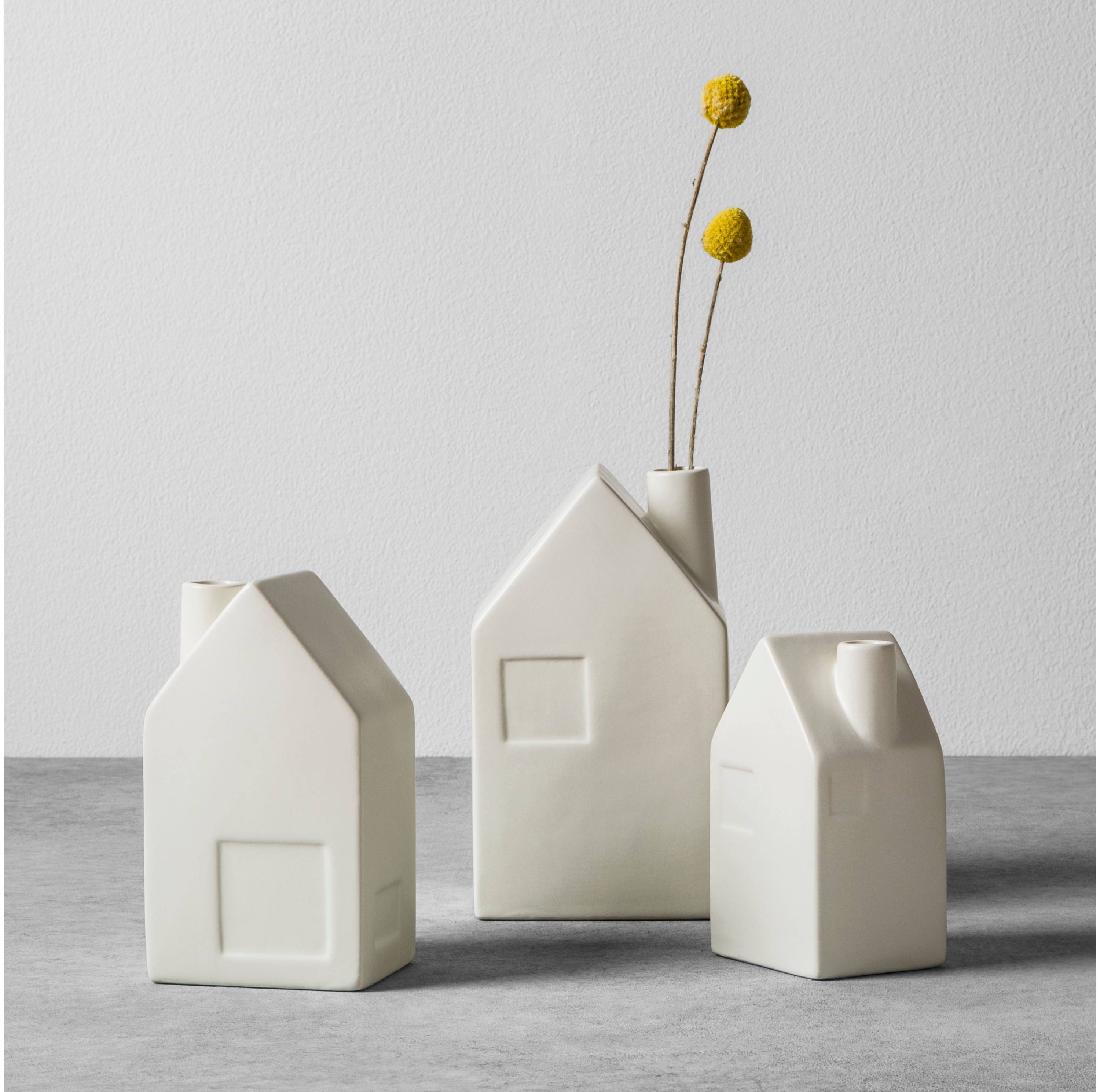 White vases that look like homes with a branch in one of them.