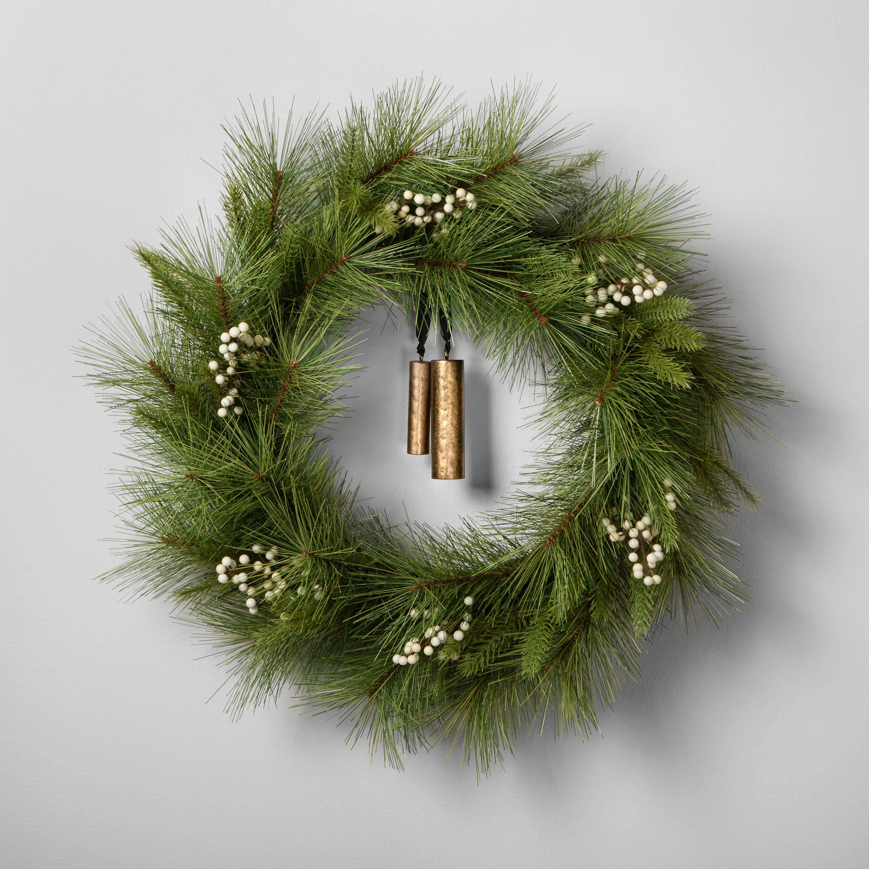 Pine wreath with white berries and a bell on the wall.