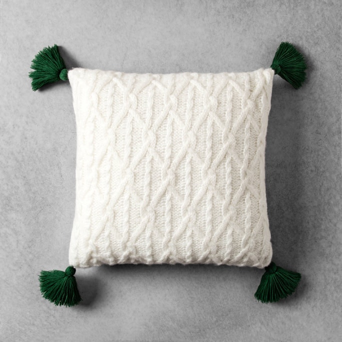 A white knit pillow with green tassels.