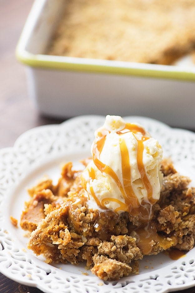 Pumpkin cobbler on a plate with ice cream on top of it, and caramel syrup drizzled.