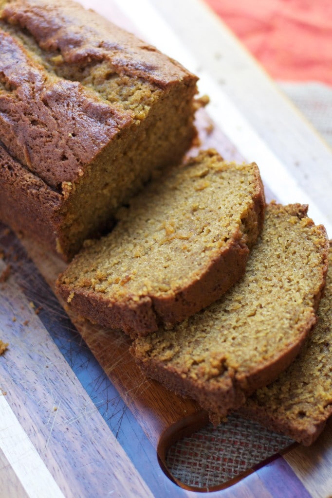 Pumpkin bread half sliced on a wooden cutting board.