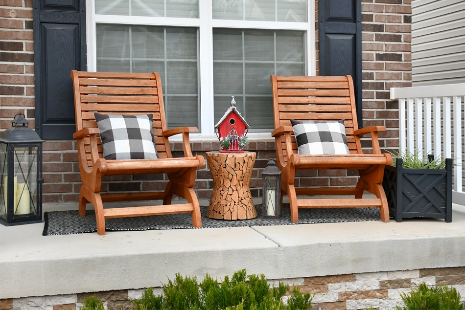 Two Adirondack chairs on the porch with a porch table in between and a candle on the porch as well.