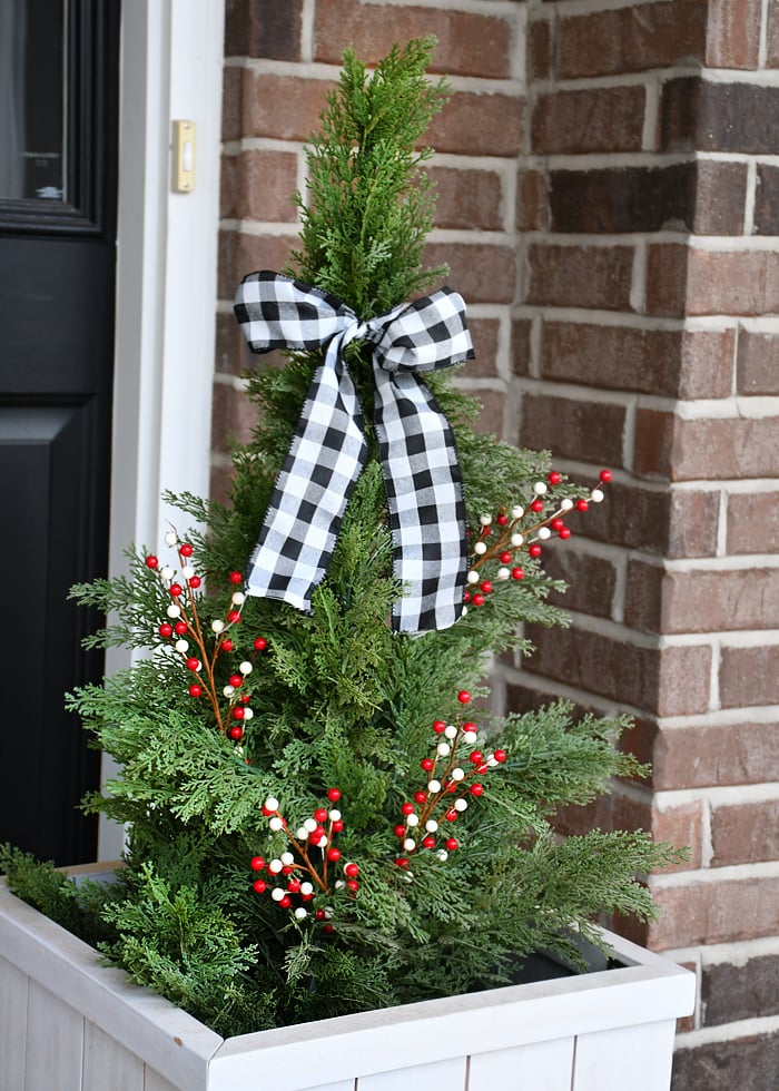 A decorated evergreen topiary with a bow tied around the top of it.