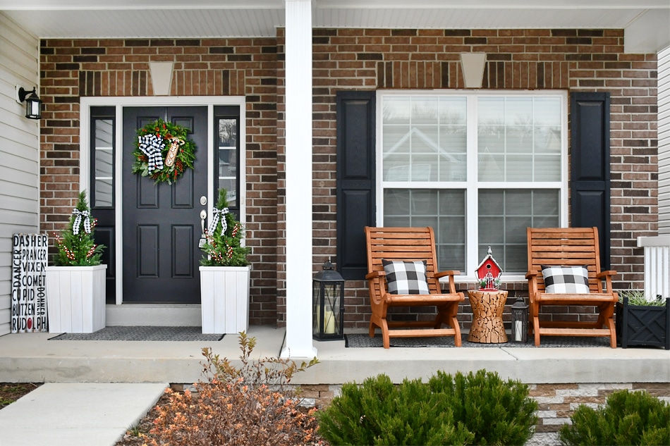 A front porch with a black door and two chairs with pillows on them.