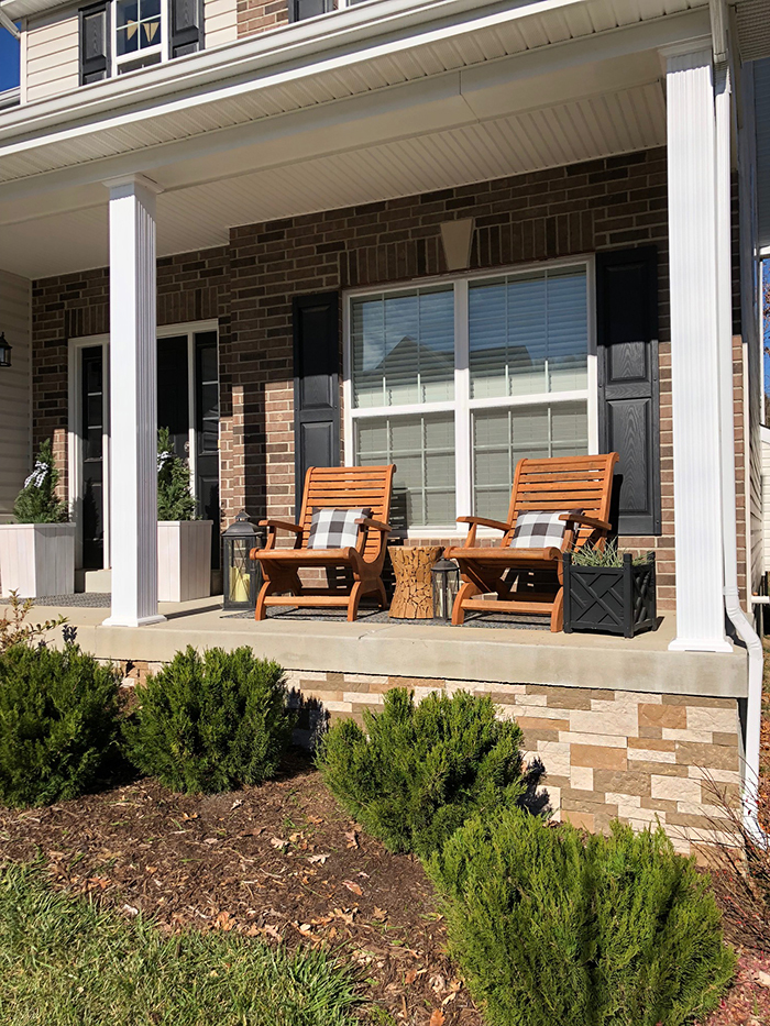 Front porch with two chairs on it and and small bushes in front.