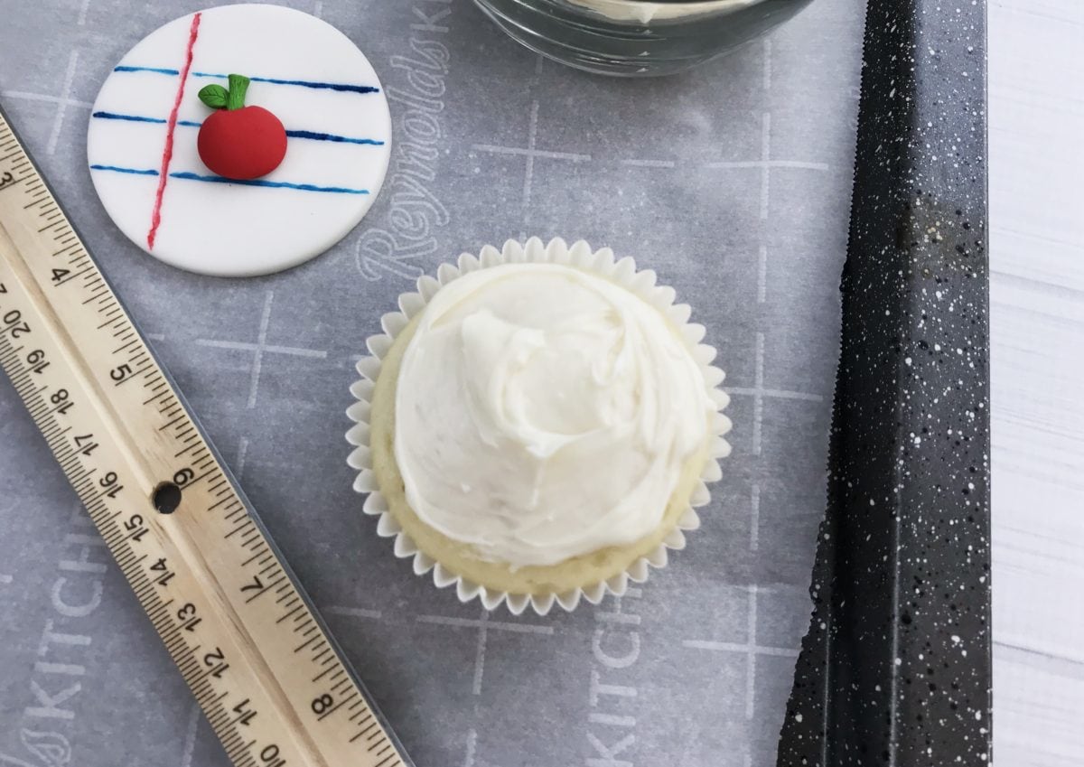 Baked cupcake with icing on it and fondant beside it with a ruler.