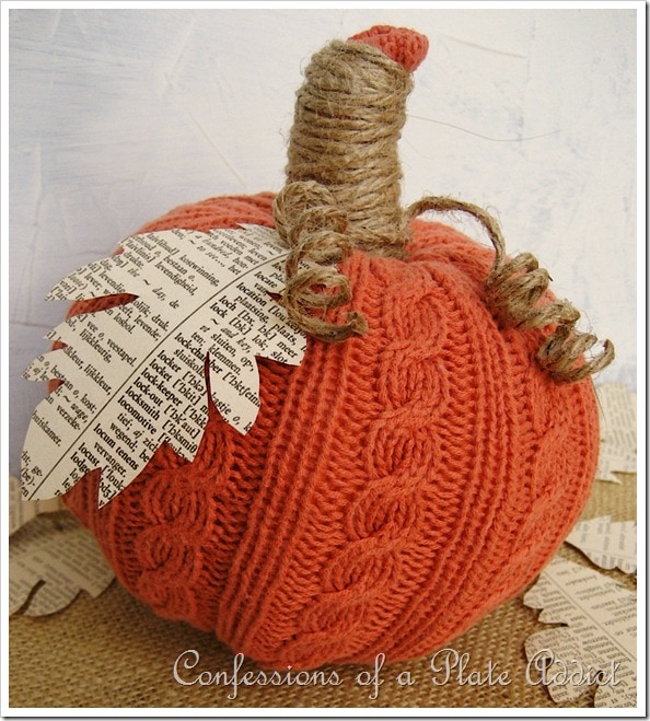 A pumpkin wrapped in an old orange sweater with a cut out leaf at stem.