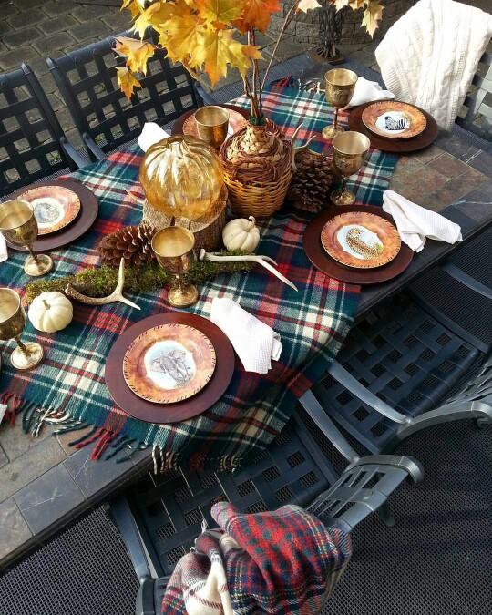 A fall table setting with a plaid runner and centrepiece with maple leaves.