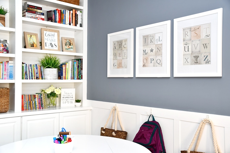 White built-in shelves are on the left frame of the photo. Various decor items and books are on the shelves. The top portion of the wall is painted Sherwin Williams Storm Cloud. The lower part of the wall is white board and batten. 3 art prints hang on the top portion of the wall.