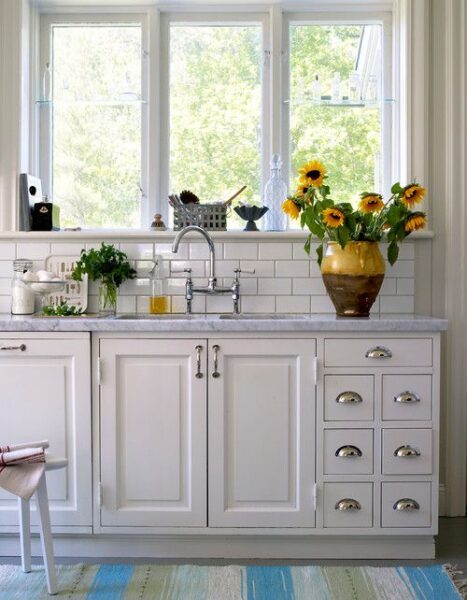 kitchen with white cabinets and white tile and a big vase with sunflowers 