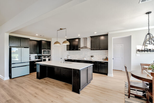 Open concept kitchen with Eider White painted walls. The kitchen cabinets are painted Tricorn Black. Countertops are a white stone. A two-light fixture hangs above the kitchen island.